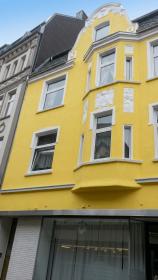 Gelb gestrichene Wohnhausfassade mit weißen Zierleisten und Schaufenster im Erdgeschoss.