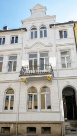Strahlend frisch gestrichene weiße Fassade mit Balkon und goldfarbenen Details, fertig renoviertes Gebäude.
