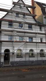 Hausfassade eingerüstet: Gerüst vor weißer Außenwand während Fassadenarbeiten, Straßenszene.