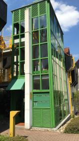 Grüner verglaster Außenturm mit Metallrahmen und Treppenhaus, moderne Fassadenanstricharbeit.