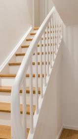 Weiß lackierte Holztreppe mit hellen Stufen und frisch gestrichenem Handlauf, seitliche Wand in warmem Weiß.